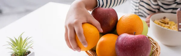 Vista ritagliata del bambino africano americano che prende arancione dal cesto di vimini con frutta fresca, banner — Foto stock