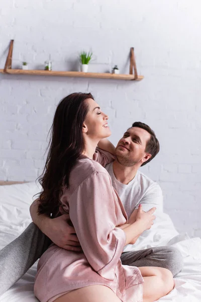 Donna sorridente in accappatoio che abbraccia il marito sul letto — Foto stock