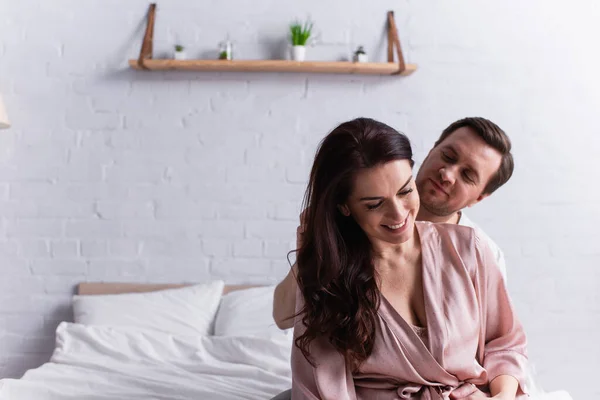 Smiling woman in robe looking away near husband in bedroom — Stock Photo