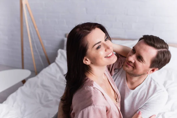 Sorrindo homem abraçando esposa na cama no fundo borrado — Fotografia de Stock
