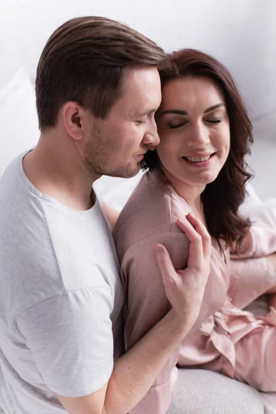 Vue grand angle de l'homme embrassant femme positive en pyjama sur le lit — Photo de stock