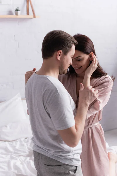 Lächelnde erwachsene Frau im Mantel umarmt Ehemann auf dem Bett — Stockfoto