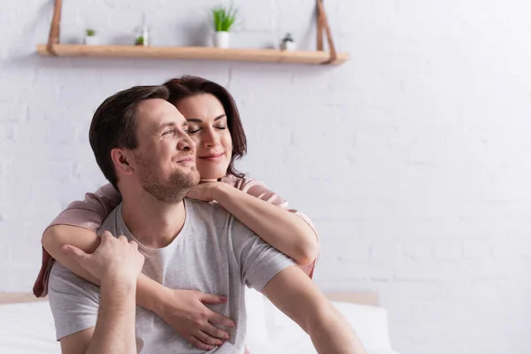 Bruna donna abbracciando sorridente marito in camera da letto — Foto stock