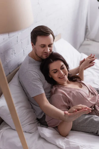 Man looking at hand of smiling wife on bed — Stock Photo