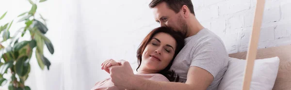 Mann hält Hand seiner Frau mit geschlossenen Augen auf Bett, Banner — Stockfoto
