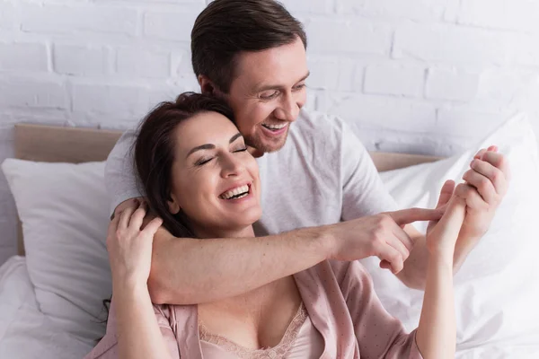 Smiling man pointing at palm of cheerful wife on bed — Stock Photo