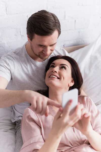 High angle view of man pointing at smartphone in hands of cheerful wife — Stock Photo