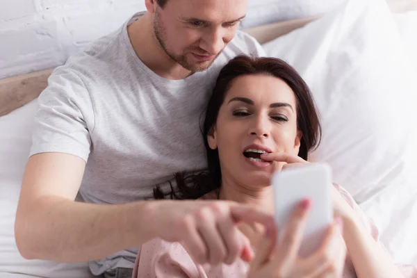Donna utilizzando smartphone in primo piano sfocato vicino al marito in camera da letto — Foto stock