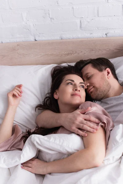 Высокий угол зрения на мужчину обнимающего жену на кровати — стоковое фото