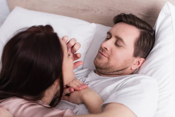 Adult man touching face of brunette wife on blurred foreground on bed — Stock Photo