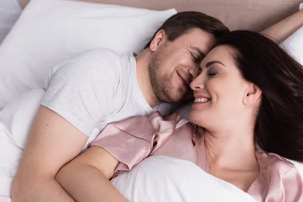 Vista superior de la mujer sonriendo cerca del marido en la ropa de cama blanca - foto de stock