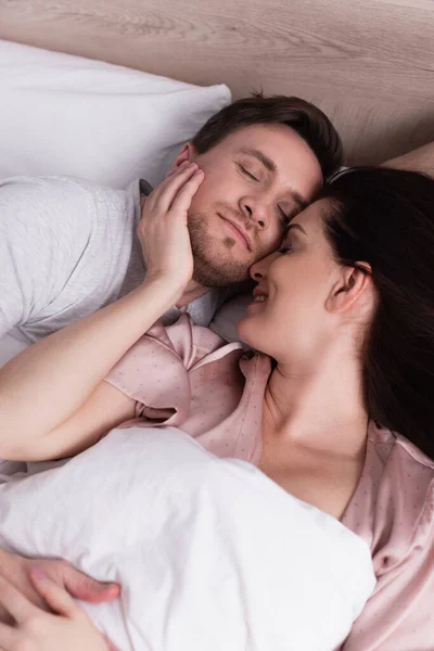 Femme souriante touchant le visage du mari endormi sur le lit — Photo de stock