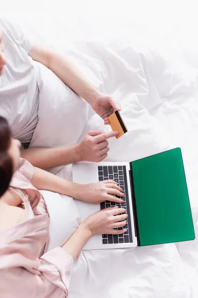 Top view of couple using laptop with green screen and credit card on bed — Stock Photo