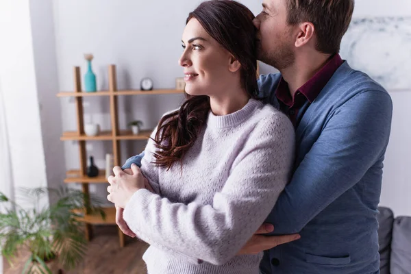 Mann küsst und umarmt lächelnde Frau im Wohnzimmer — Stockfoto