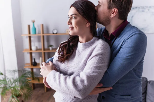 Hombre besándose y abrazando sonriente esposa en sala de estar - foto de stock