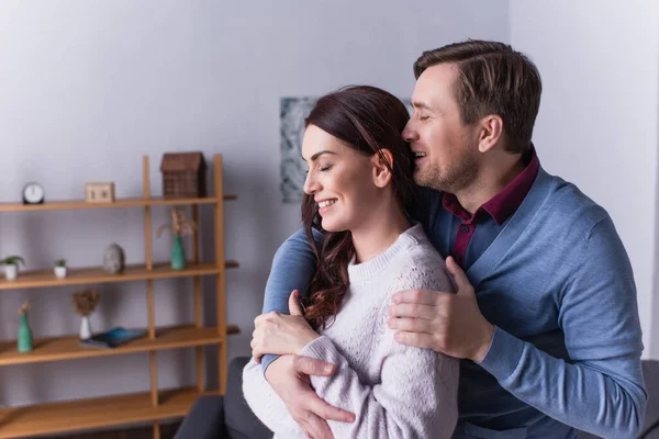 Homme souriant étreignant femme en pull à la maison — Photo de stock