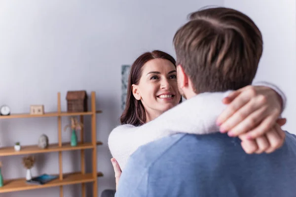 Donna adulta sorridente mentre abbraccia il marito in primo piano sfocato a casa — Foto stock