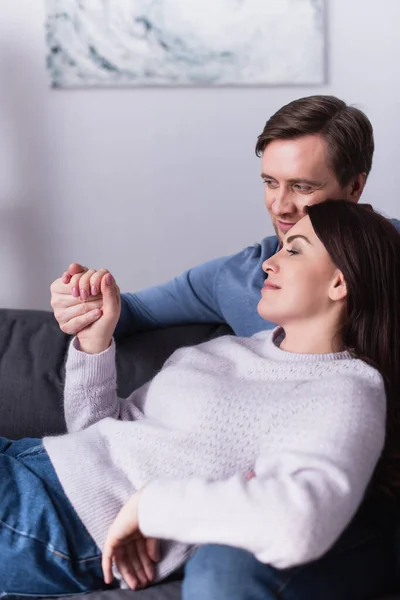 Woman holding hand of smiling husband on couch — Stock Photo