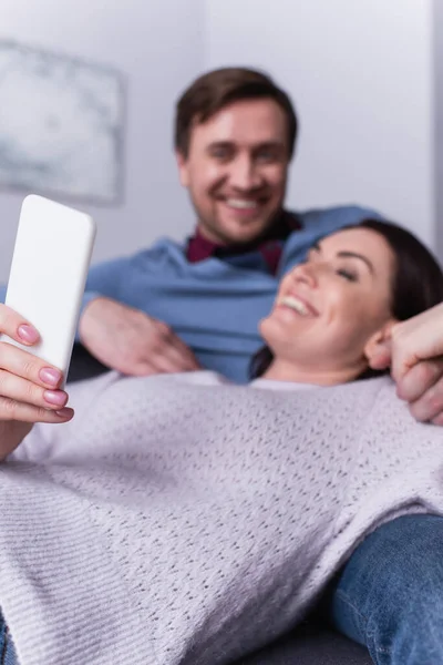 Жінка використовує мобільний телефон біля чоловіка на розмитому фоні — стокове фото