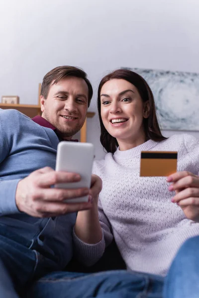 Adult couple using smartphone and credit card on blurred foreground — Stock Photo