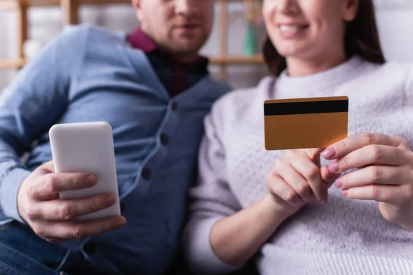 Vista recortada del teléfono celular y la tarjeta de crédito en manos de la pareja sobre fondo borroso - foto de stock
