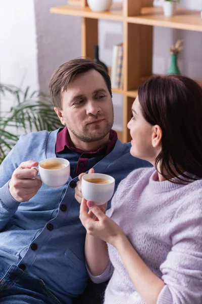Hombre con taza de café mirando a la esposa en primer plano borroso - foto de stock