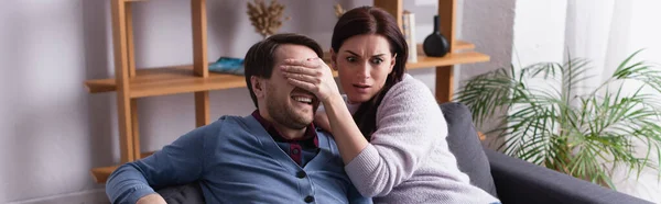 Donna spaventata che copre gli occhi al marito sul divano, striscione — Foto stock