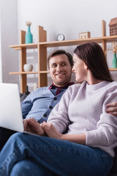 Homme souriant étreignant femme avec ordinateur portable sur le premier plan flou — Photo de stock