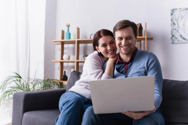 Feliz pareja adulta utilizando el ordenador portátil en el sofá - foto de stock