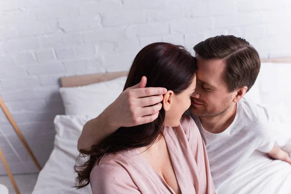 Uomo adulto che tocca i capelli della moglie bruna in pigiama sul letto — Foto stock