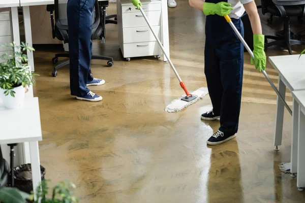 Vista recortada de limpiadores lavando piso en la oficina - foto de stock