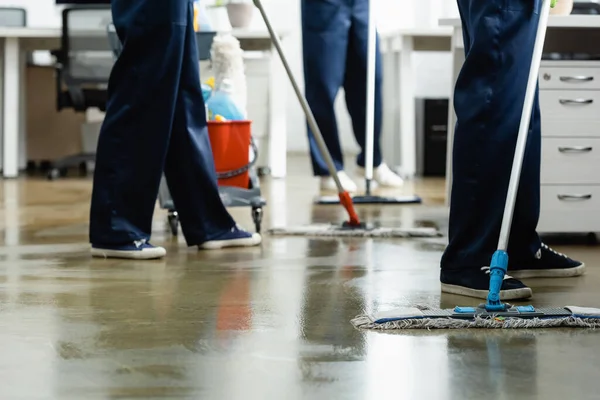 Vista recortada de limpiadores lavando piso con fregonas en la oficina - foto de stock