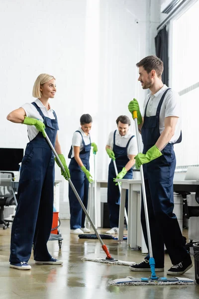 Lächelnde Putzfrau im Gespräch mit Kollegin beim Fußbodenwaschen im Büro — Stockfoto