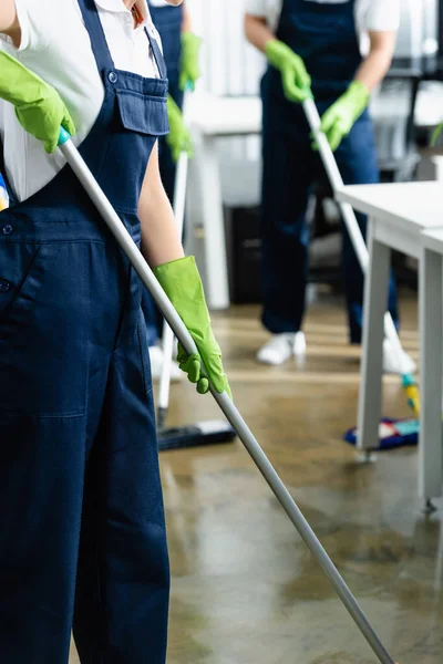 Cropped view of cleaner in rubber gloves holding mop in office on blurred background — Stock Photo