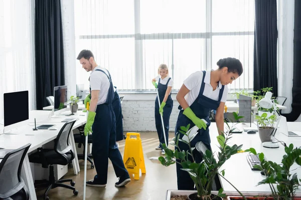 Multiethnische Reinigungskräfte arbeiten im Büro mit Reinigungsmitteln — Stockfoto