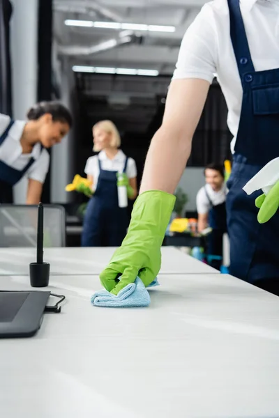 Trabajador de la empresa de limpieza de la mesa de lavado con detergente cerca de tableta gráfica en la mesa - foto de stock