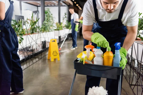 Trabajador de detergente de apertura de servicio de limpieza cerca de colegas en la oficina - foto de stock