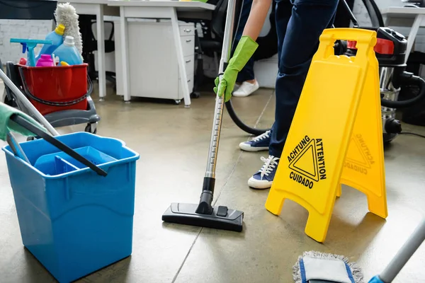 Cropped view of cleaner using vacuum cleaner near wet floor signboard in office — Stock Photo