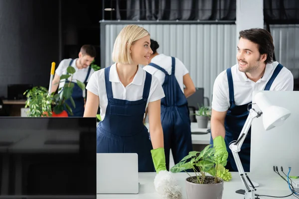 Nettoyeurs souriants parlant près de la table avec des ordinateurs dans le bureau — Photo de stock