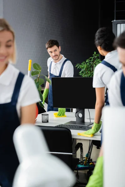 Cleaner looking at african american colleague cleaning table in office — Stock Photo