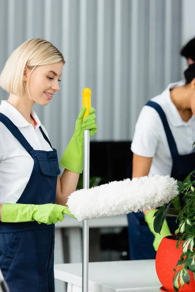 Cleaner holding mop and dust brush near plant in office — Stock Photo