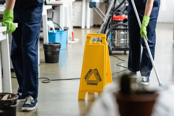 Cropped view of wet floor signboard near cleaners working in office — Stock Photo