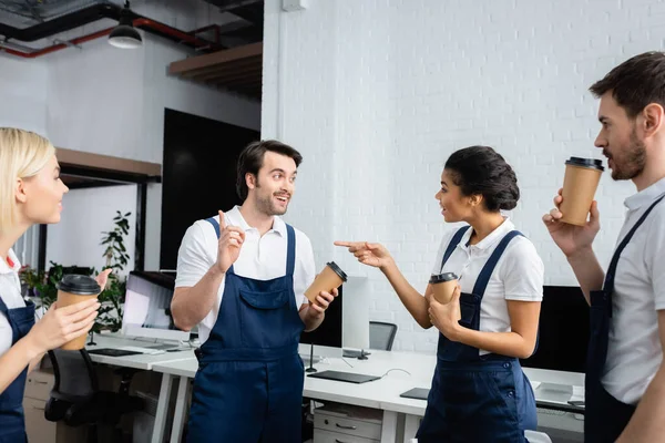 African american cleaner with coffee to go pointing at colleague in office — Stock Photo