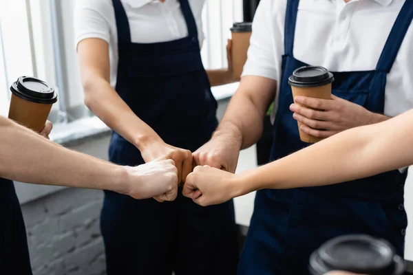 Cropped view of workers of cleaning company with coffee to go doing fists bump in office — Stock Photo
