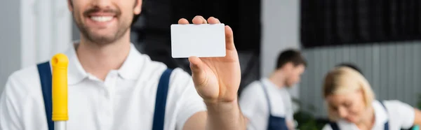 Tarjeta vacía en la mano de limpiador sonriente sobre fondo borroso en la oficina, pancarta - foto de stock