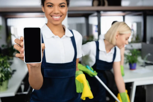 Smartphone en mano de limpiador afroamericano sobre fondo borroso en la oficina - foto de stock