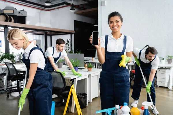 African american cleaner holding smartphone with copy space near colleagues working in office — Stock Photo