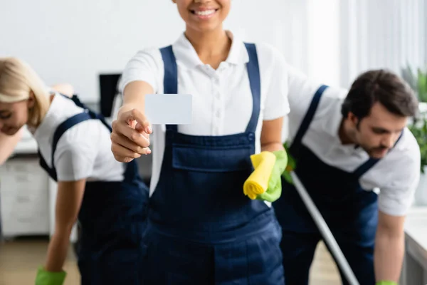 Empty card in hand of african american cleaner near colleagues in office — Stock Photo