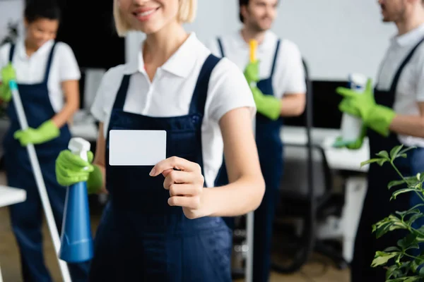 Empty card in hand of cleaner with detergent on blurred background in office — Stock Photo