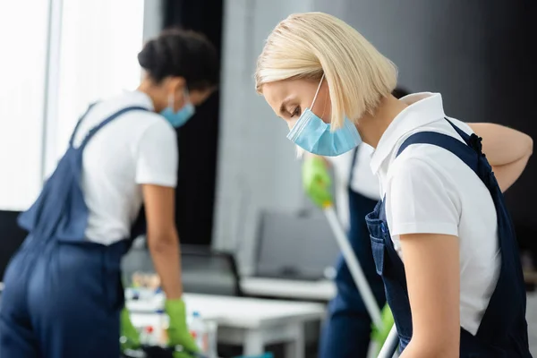 Reinigungskraft in medizinischer Maske arbeitet neben Kollegen im Büro — Stockfoto